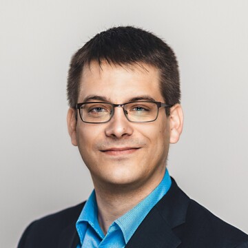 Philipp Zumstein hat kurzes braunes Haar. Er trägt eine Brille, ein blaues Hemd und ein dunkles Jackett.