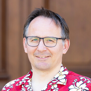 Jörg Mechnich hat kurzes braungraues Haar, er trägt eine Brille und ein rotes Hemd mit froralen Mustern in Weiß und Schwarz.