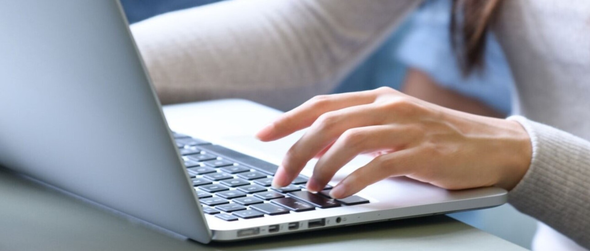 Eine Studentin schreibt an einem Laptop, im Bild sind die Arme, die linke Hand am Laptop, der Oberkörper und lange braune Haare. Das Laptop steht auf einem Tisch im ExpLAB im Bibliotheksbereich Schloss Schneckenhof.