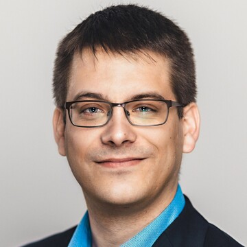 Philipp Zumstein hat kurzes braunes Haar. Er trägt eine Brille, ein blaues Hemd und ein schwarzes Jackett.