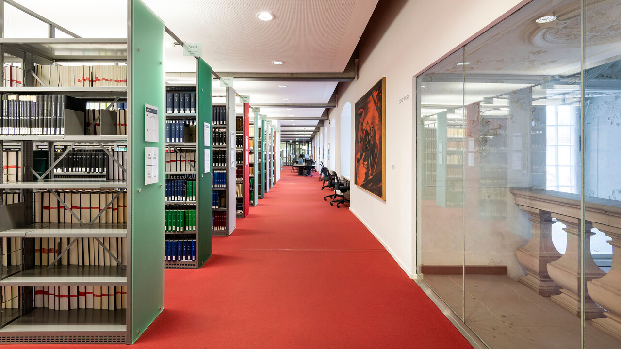 Langer Gang entlang von Bücherregalreihen im Bibliotheksbereich Schloss Ehrenhof.