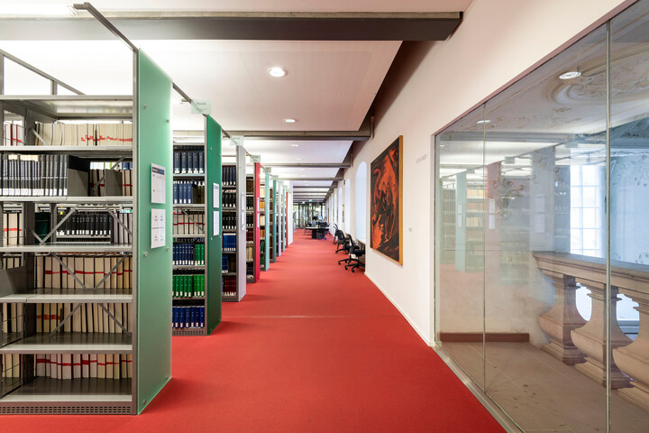 Langer Gang entlang von Bücherregalreihen im Bibliotheksbereich Schloss Ehrenhof.