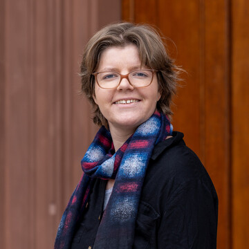 Vanessa Kolb hat braunes lockiges Haar. Sie trägt eine Brille, eine dunkle Jacke und einen Schal.