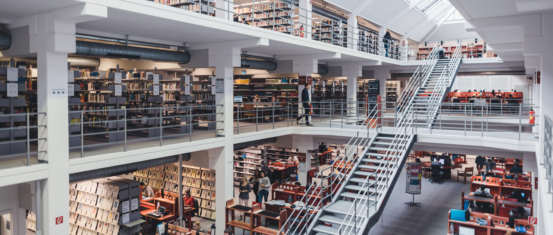 Blick in den Bibliotheksbereich A3 mit Galerien, großer Treppe, Bücherregalen und Arbeitsplätzen.