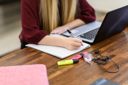 Online-Lehre in der Universität Studentin sitzt vor ihrem Laptop und ihren Schreibunterlagen und macht sich Notizen.