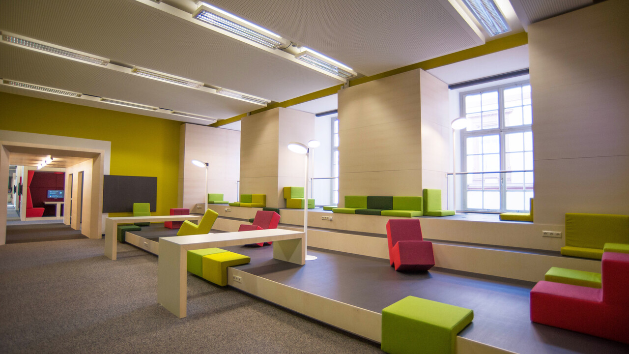 Die Lounge im Bibliotheksbereich Schloss Schneckenhof mit Podesten zum Sitzen, Sesseln, Sitzkissen und kleinen Tischen.