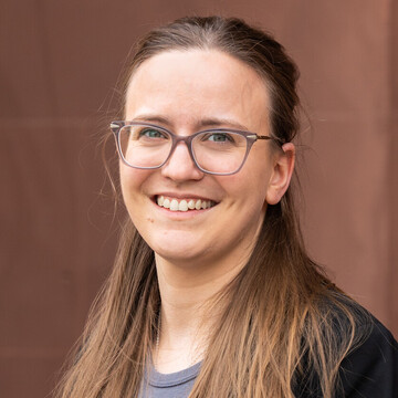 Lucia Oberhollenzer hat langes hellbraunes Haar. Sie trägt eine Brille, ein blaues Oberteil und ein schwarzes Jacket. 