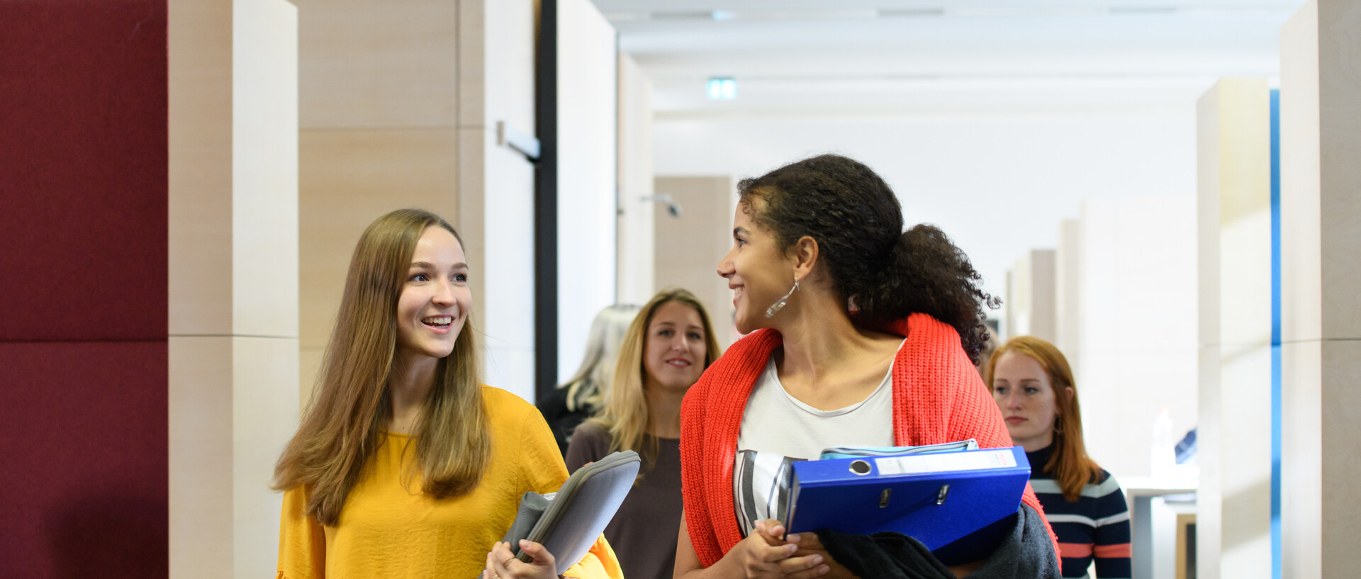 Eine Gruppe Studierender läuft durch das Learning Center im Bibliotheksbereich Schloss Schneckenhof. Sie haben Laptop, Ordner, Collegeblock und Stiftemäppchen dabei.