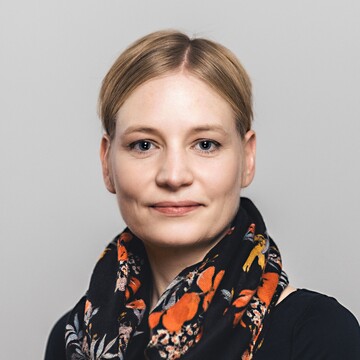 Marion von Francken-Welz hat kurzes blondes Haar. Sie trägt ein schwarzes Halstuch mit floralem Muster und ein schwarzes Oberteil.