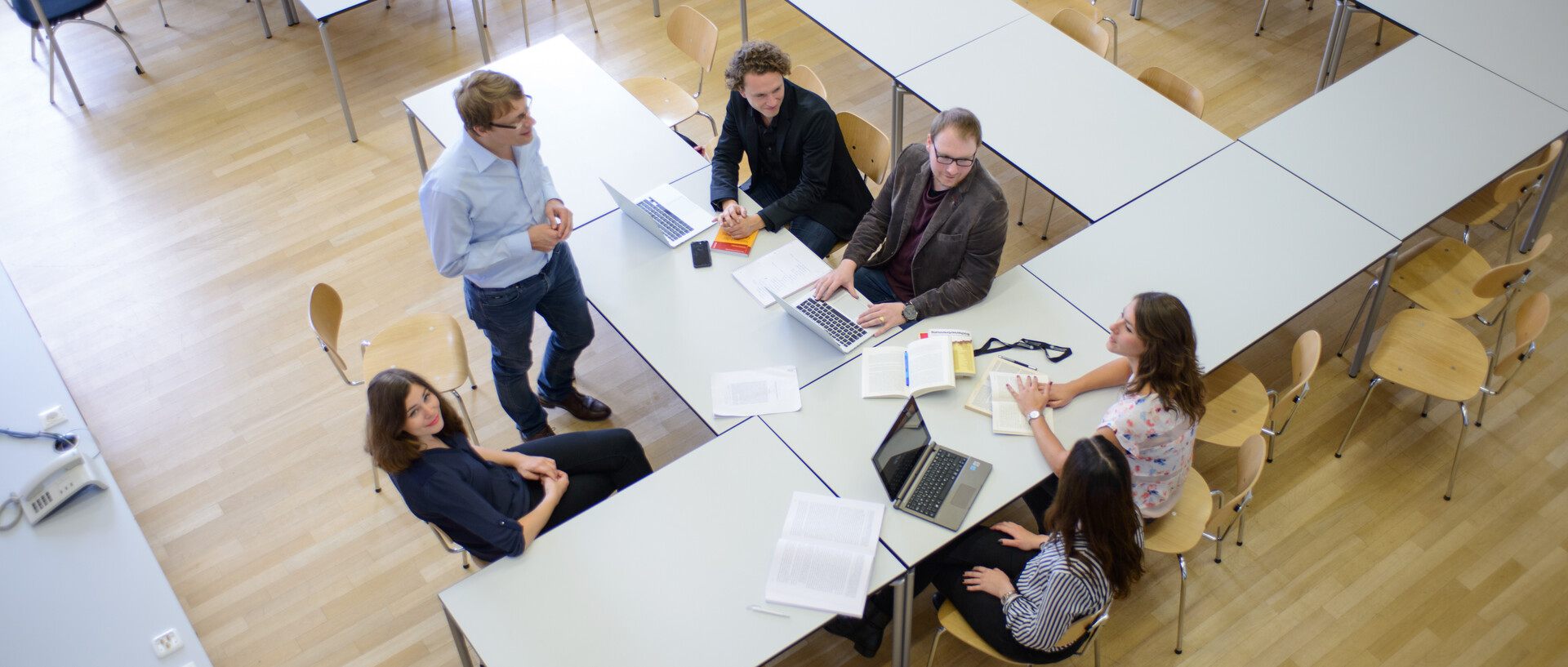 Sechs Personen arbeiten gemeinsam in einem Seminarraum. Im Raum stehen Schreibtische und Laptops.