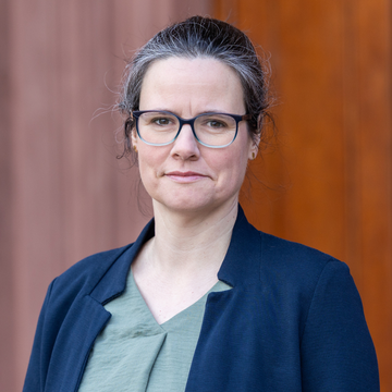 Dr. Regina Jutz hat braunes Haar, sie trägt eine Brille, eine grüne Bluse und ein dunkelblaues Jacket.