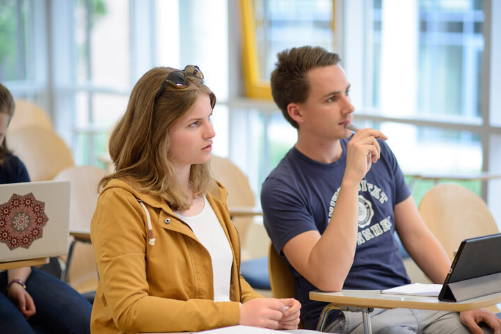 Zwei Studierende sitzen nebeneinander. Sie schauen konzentriert nach vorne.