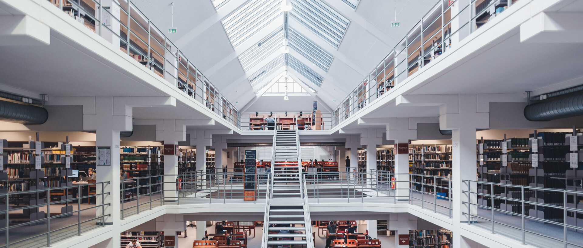 Blick in den Bibliotheksbereich A3 mit Galerien, großer Treppe, Bücherregalen und Arbeitsplätzen.